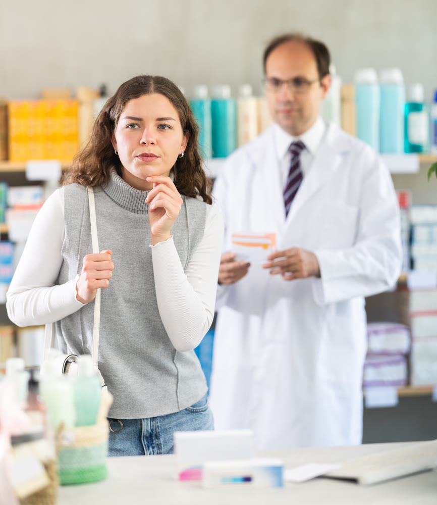 Female customer chooses medicines in drugstore. Pharmacist helps her