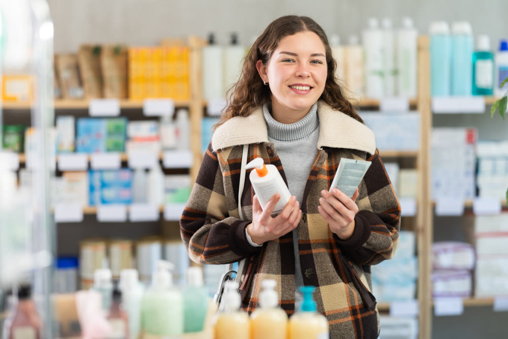Girl in winter clothes choosing skin cream at drugstore