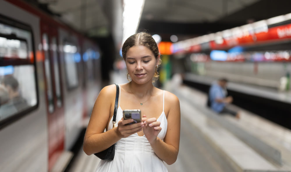 Young woman standing on platform near train with mobile phone