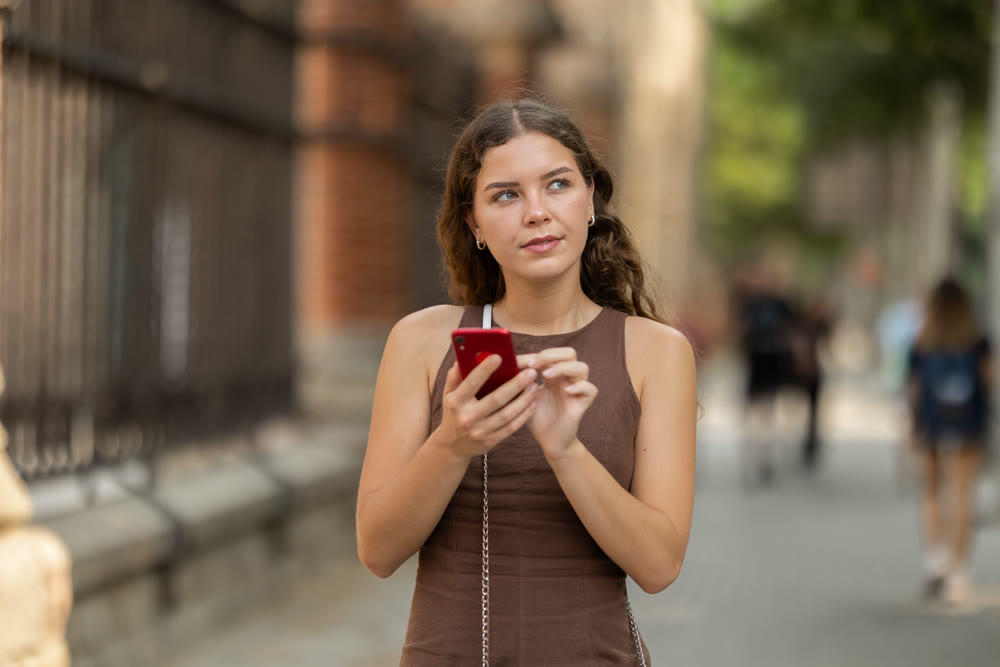 Positive young woman watching her smartphone during walking near architectural complex of Hospital de la Santa Creu i Sant Pau during of Barcelona