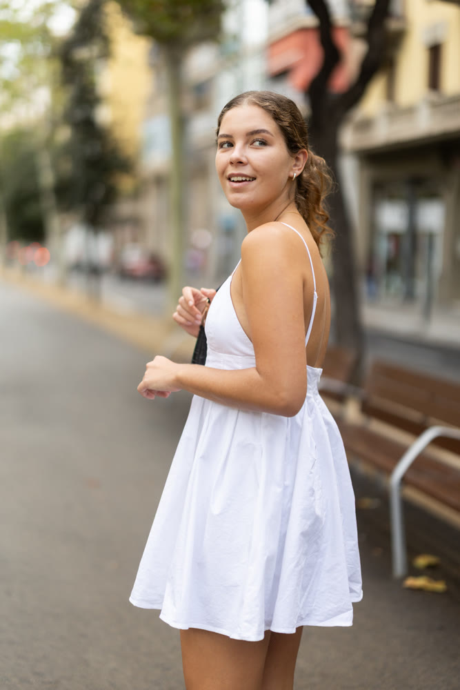 Young girl in white summer dress walking along quiet city street