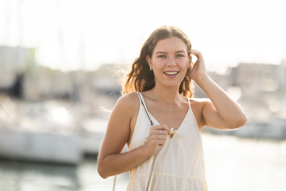 Happy young woman walking along the seaside promenade admiring city and yachts