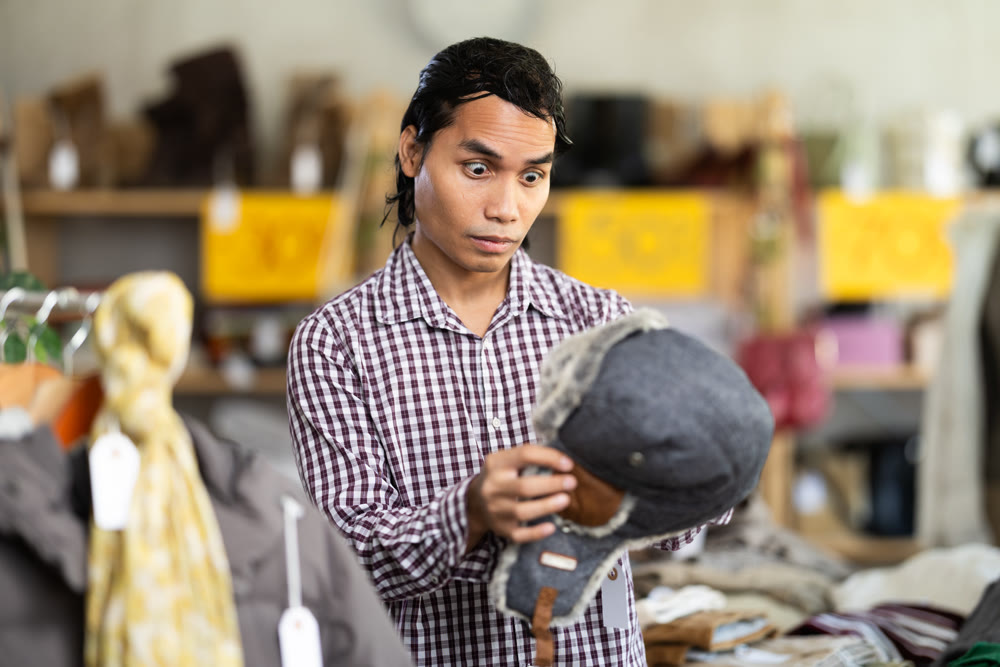 In chain shop, amazed Indonesian man choose hat cap with earflaps