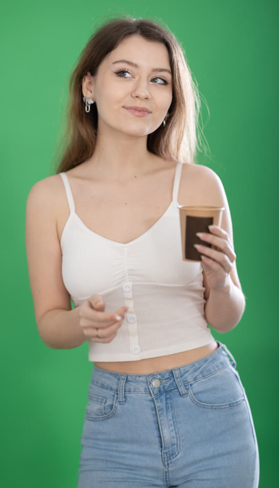 Chroma key compositing. Pretty young woman drinking coffee and scrolling through her smartphone screen against green screen background.