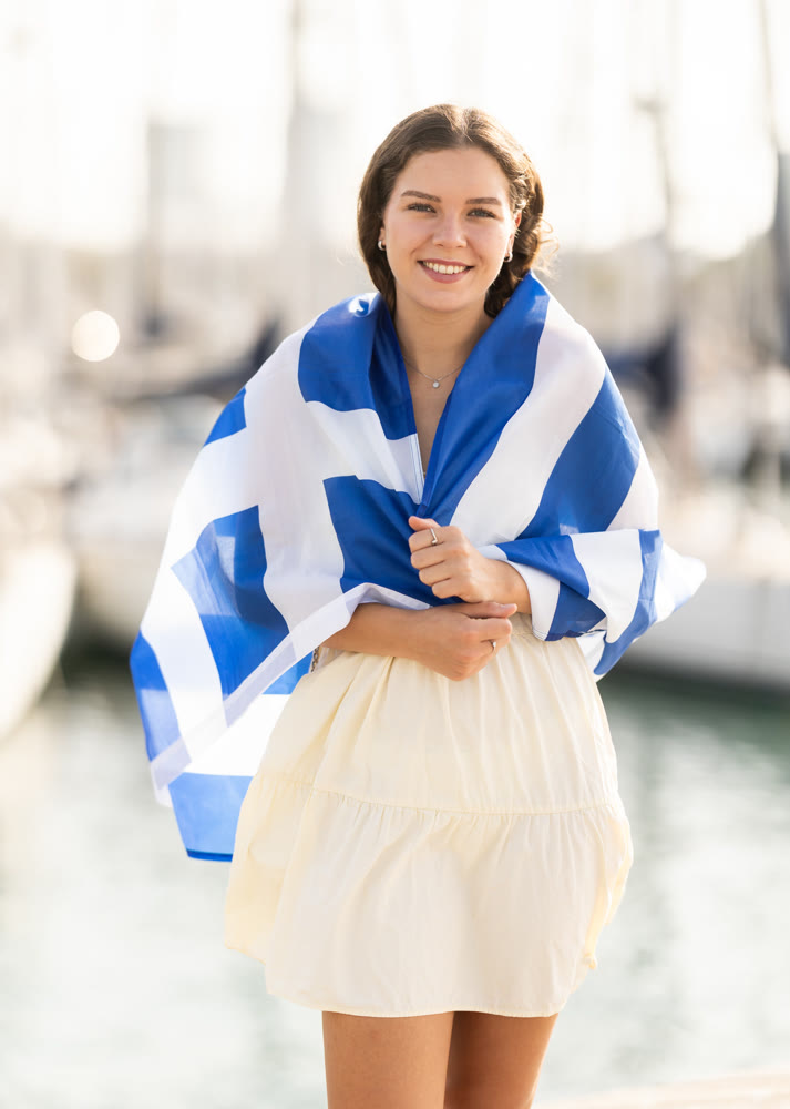 Young woman wrapped in Greek flag at port