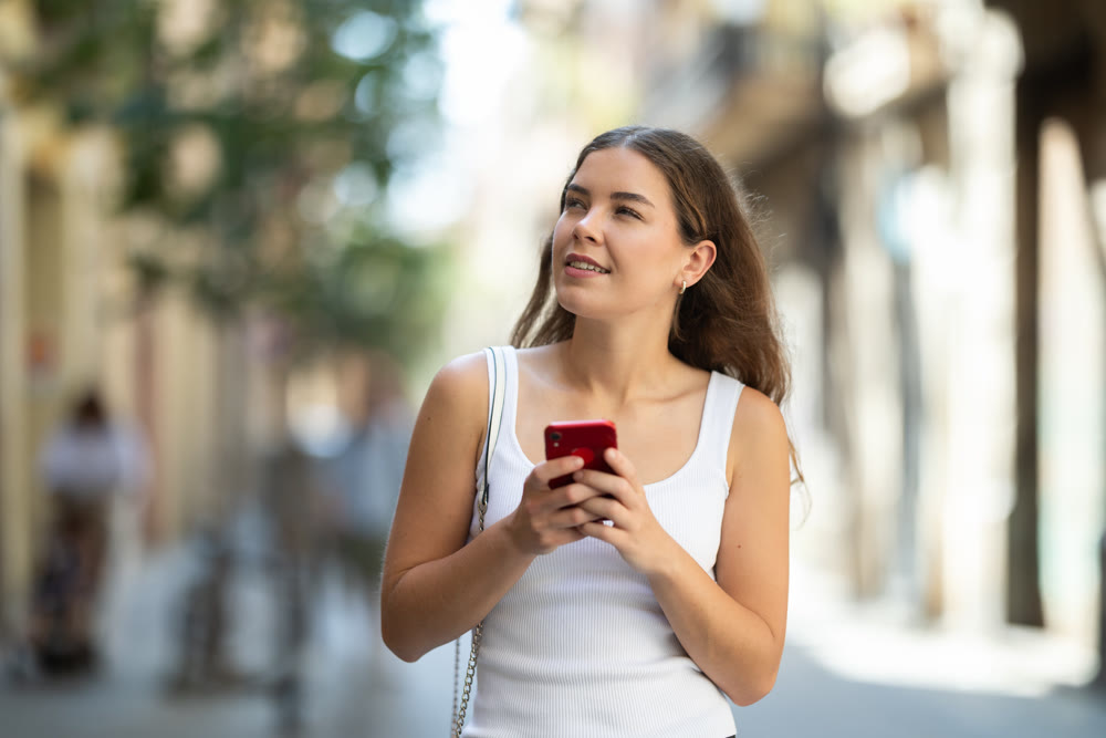 Young woman checking phone while walking in summer city