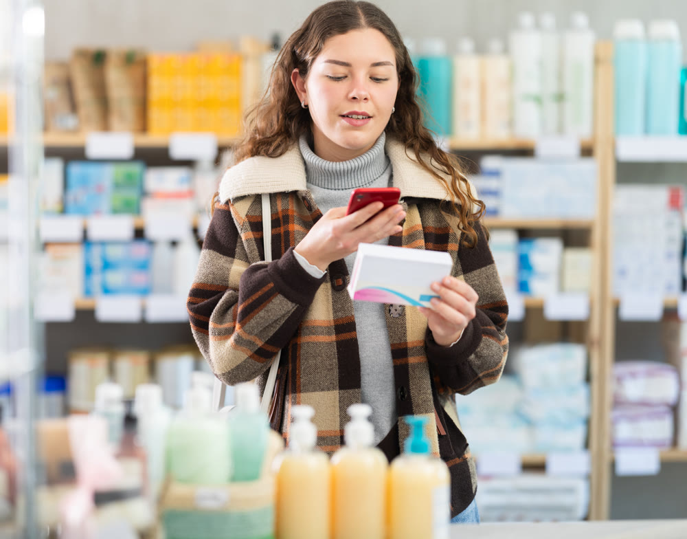 Girl in winter clothes scans code on package of pills to check expiration date