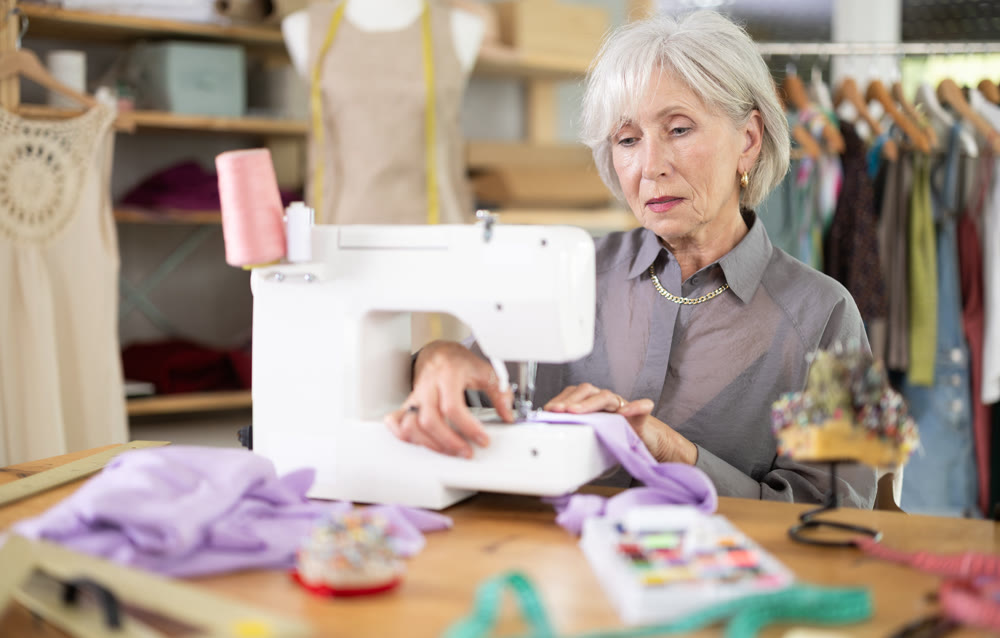 Mature female dressmaker working with sewing-machine in tailor's workshop