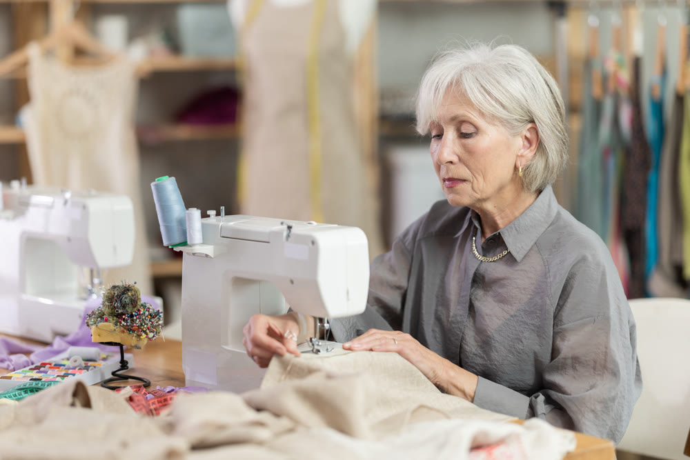 Mature female dressmaker working with sewing-machine in tailor's workshop