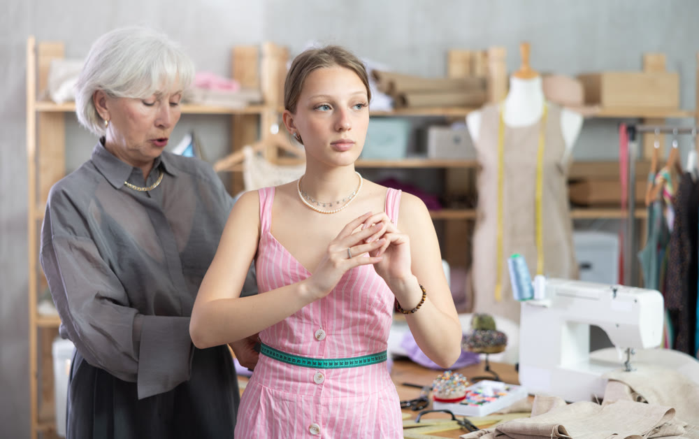 Mature tailoress measuring female client in sewing workshop