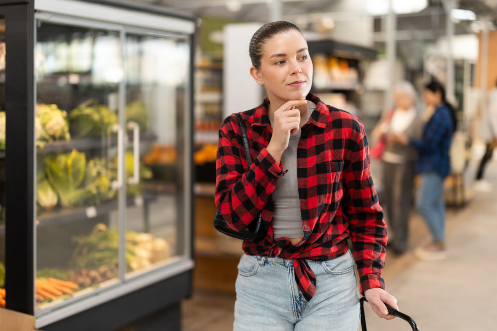 Visiting store woman is looking at something on shelf of showcase, client buy goods