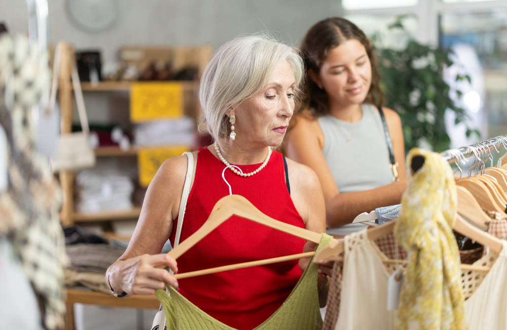 Two happy women of different ages choose summer clothes in fashion boutique