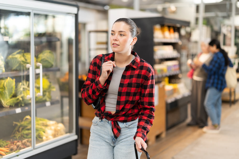 Visiting store woman is looking at something on shelf of showcase, client buy goods