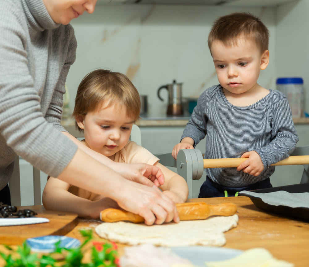 Mother and two young boys making pizza together in home kitchen