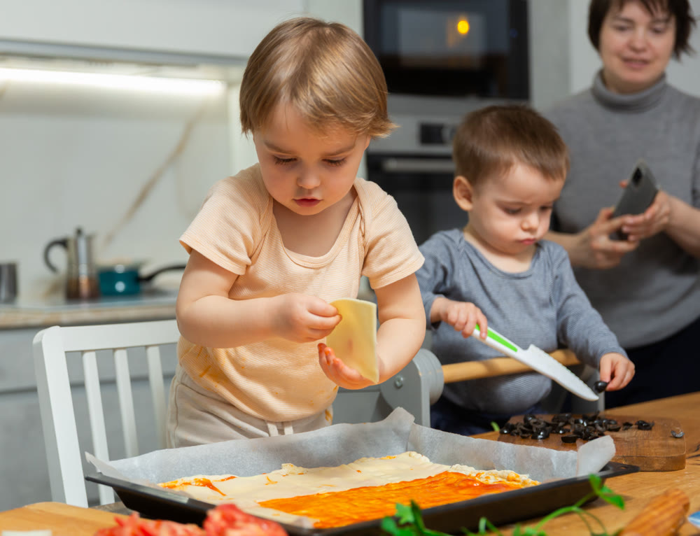 Family are cooking pizza together in cozy home kitchen. Cute kids with happy mother are preparing food or meal for dinner