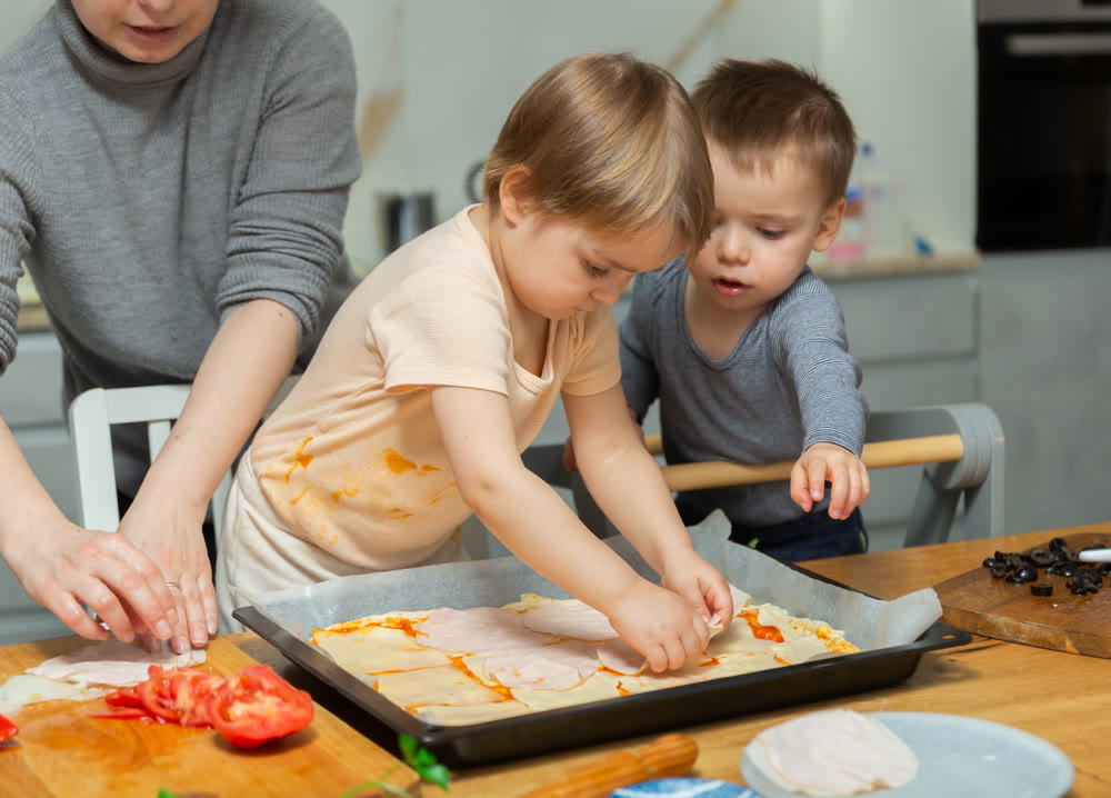 Family are cooking pizza together in cozy home kitchen. Cute kids with happy mother are preparing food or meal for dinner