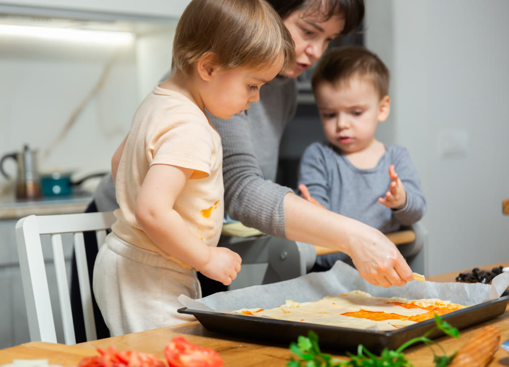 Family are cooking pizza together in cozy home kitchen. Cute kids with happy mother are preparing food or meal for dinner