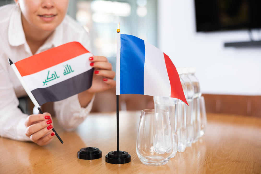 Flags of Iraq and France stand on negotiating table in office