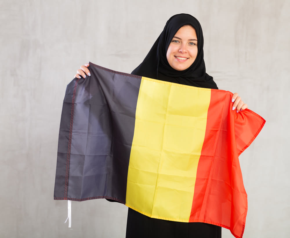 smiling Muslim woman in traditional black hijab holds flag of Belgium