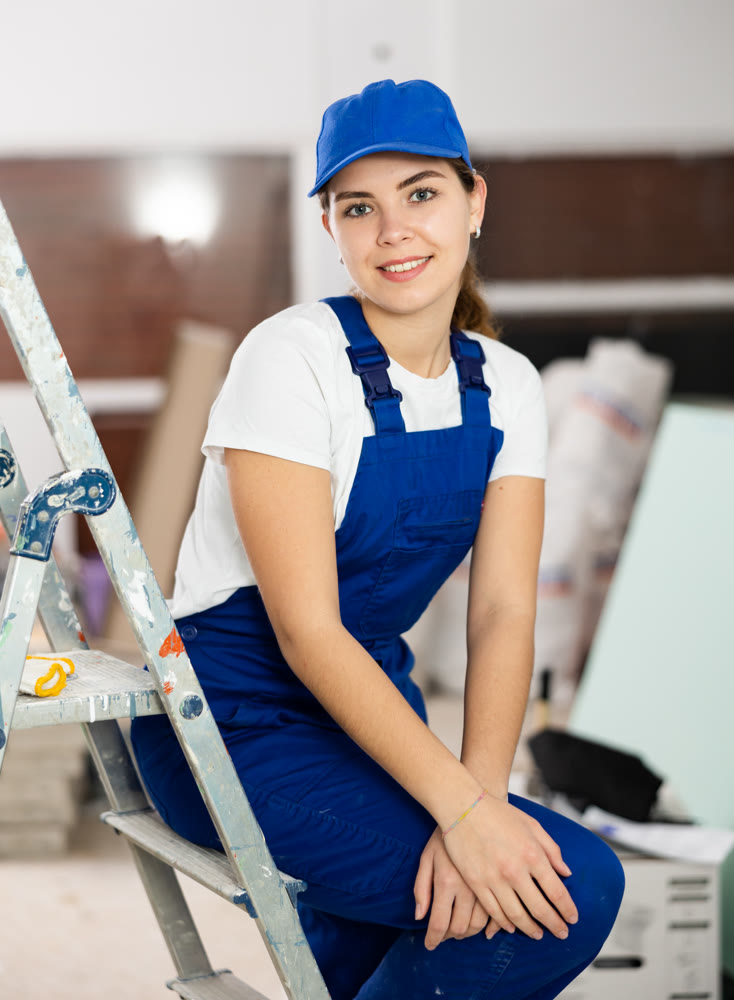 Positive builder woman in blue overalls next to stepladder
