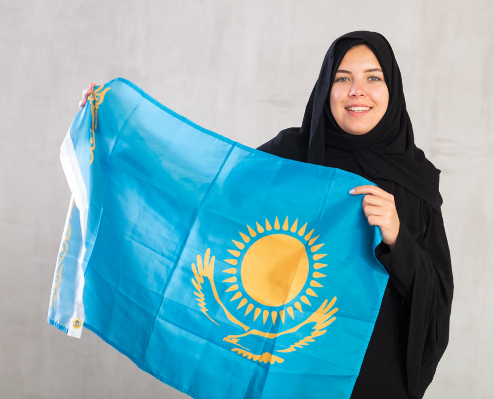 Smiling joyful Muslim woman in traditional black hijab holds flag of Kazakhstan