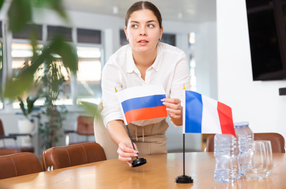 Employee of delegation prepares negotiating table - sets up flag of Russia and France