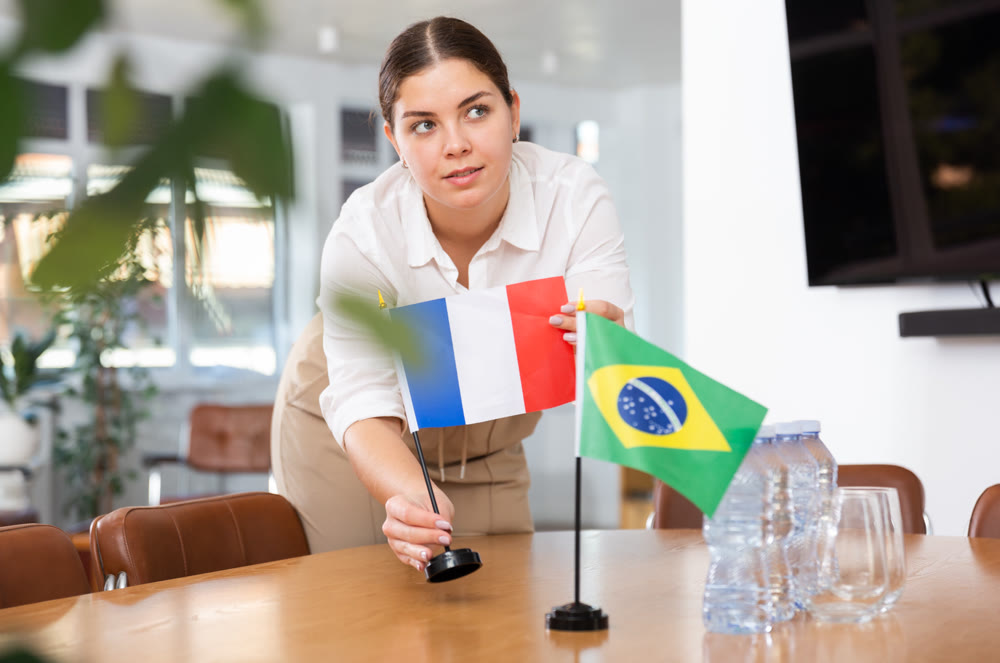 Young female assistant putting up brazilian and french flags on table for international negotiations
