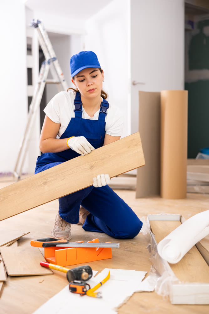Woman builder puts laminate on the floor in room