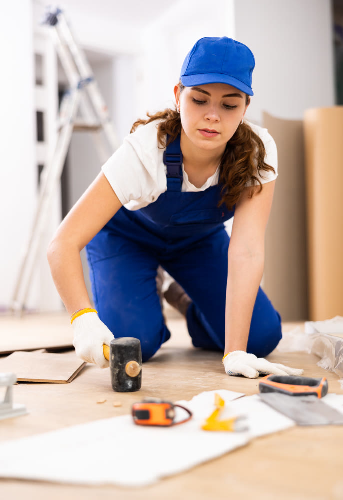 Woman builder puts laminate on the floor in room