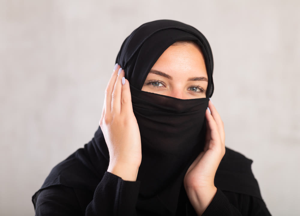 Muslim woman with face covered with burka holds thin fabric of yashmak with her hands