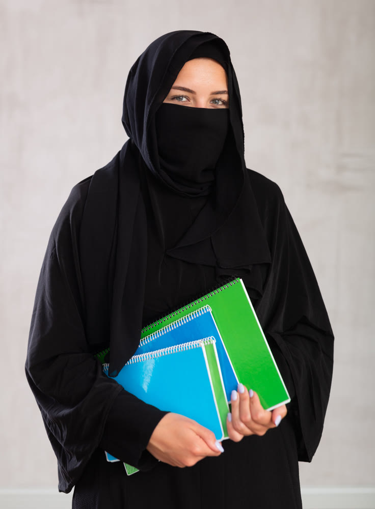 girl with face covered with burka holds lot of thick notebooks. foreign