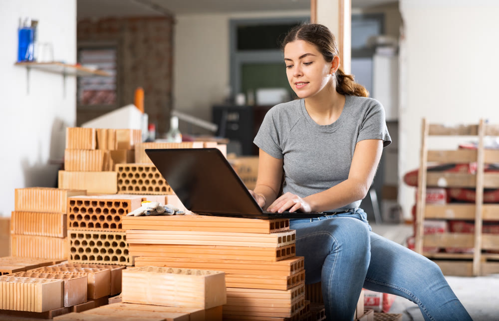 Female designer working with laptop in apartment under renovation