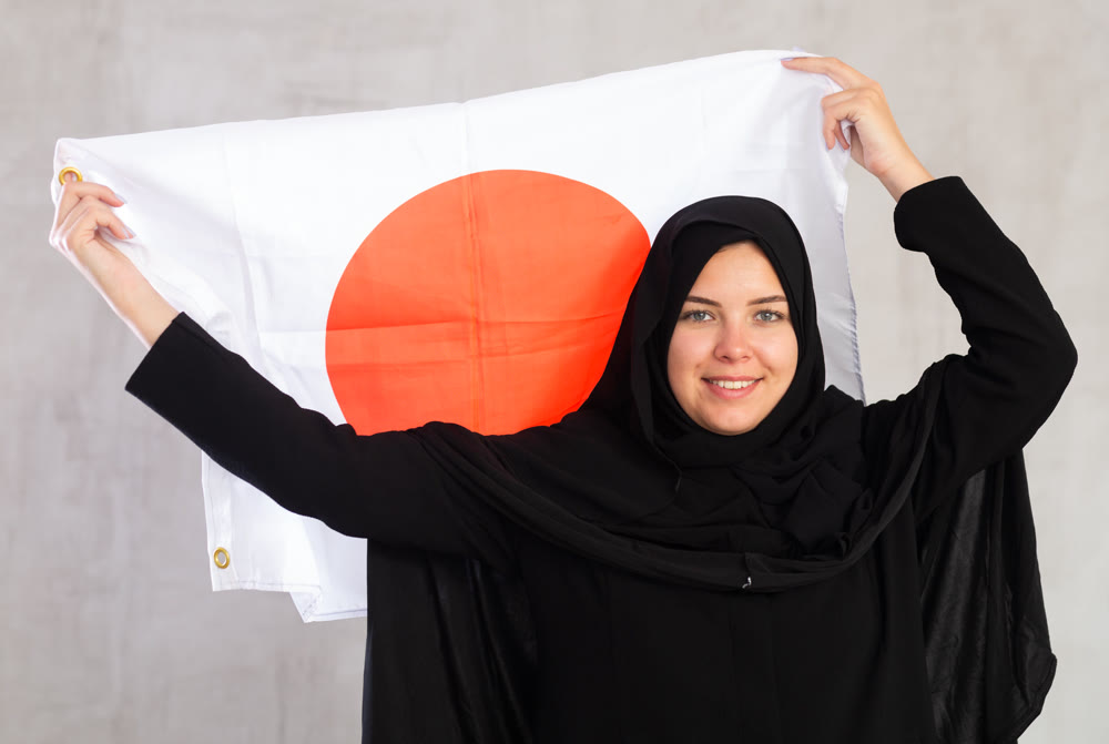 Happy young woman dressed in traditional islamic clothes with japanese flag