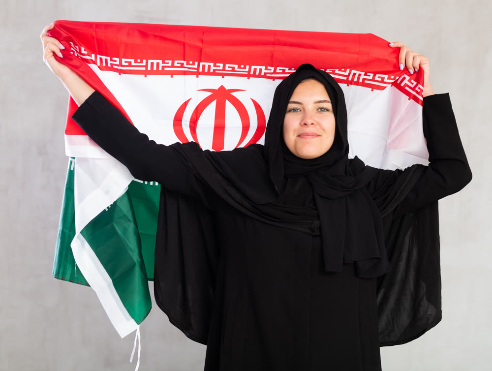 Balanced smiling Muslim woman in traditional black hijab holds flag of Iran