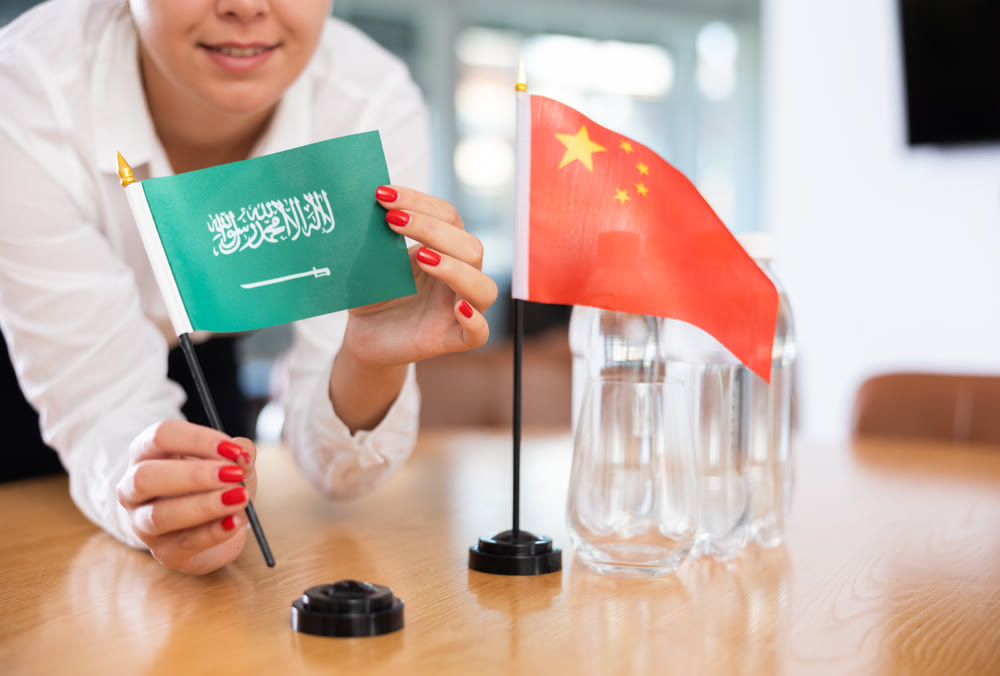 Young woman putting flags of China and Saudi Arabia on table in office