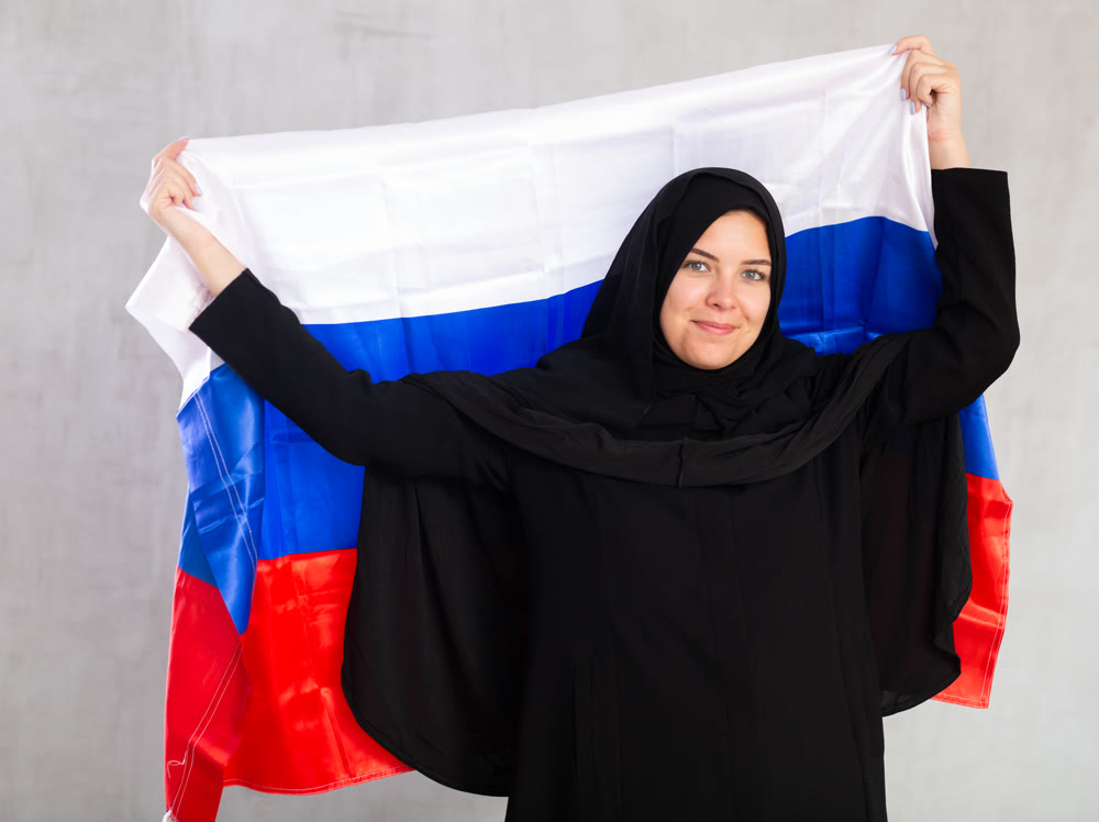 Balanced smiling Muslim woman in traditional black hijab holds flag of Russia