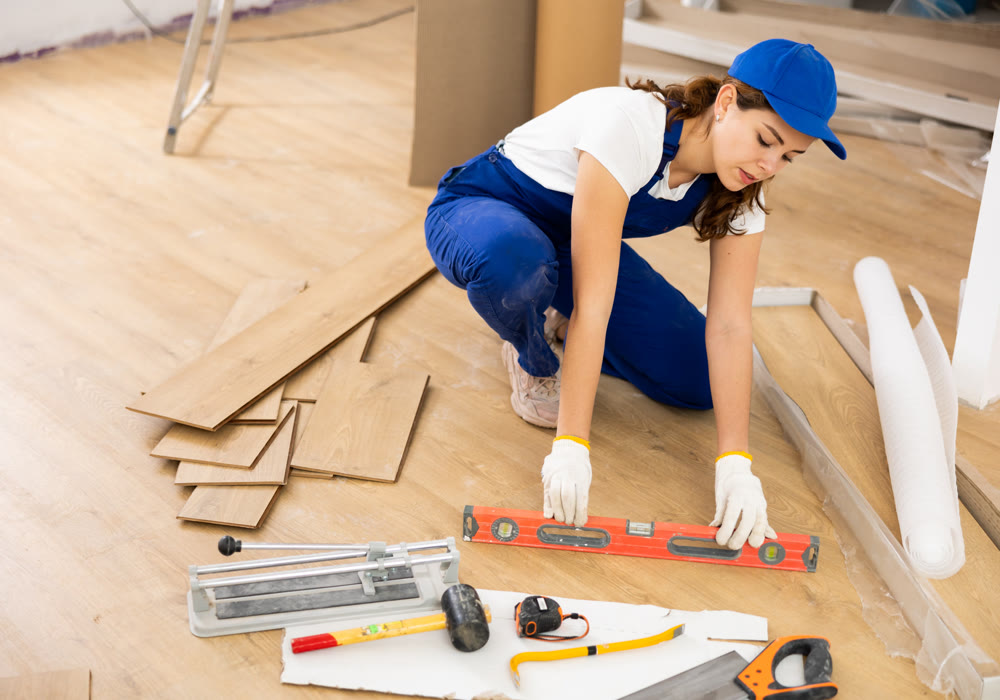Woman builder puts laminate on the floor in room