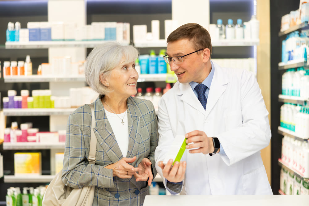 Elderly woman client consults with pharmacist which medicinal ointment to buy