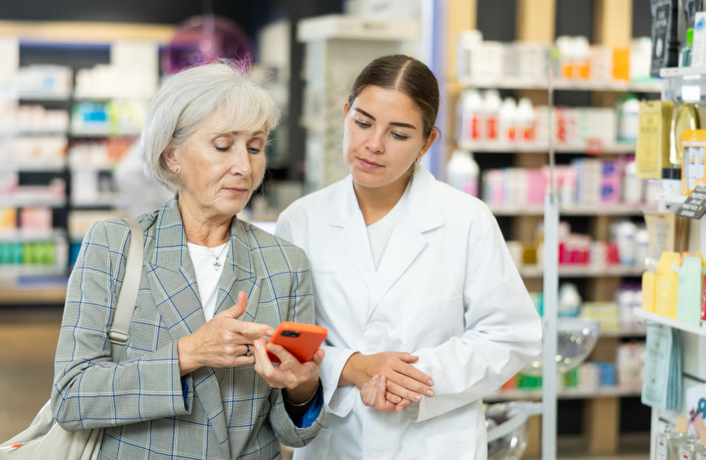 Old female customer asking young chemist about product reflected on her phone
