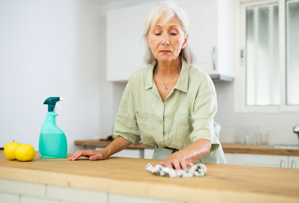 Elderly woman washing kitchen table during cleanup