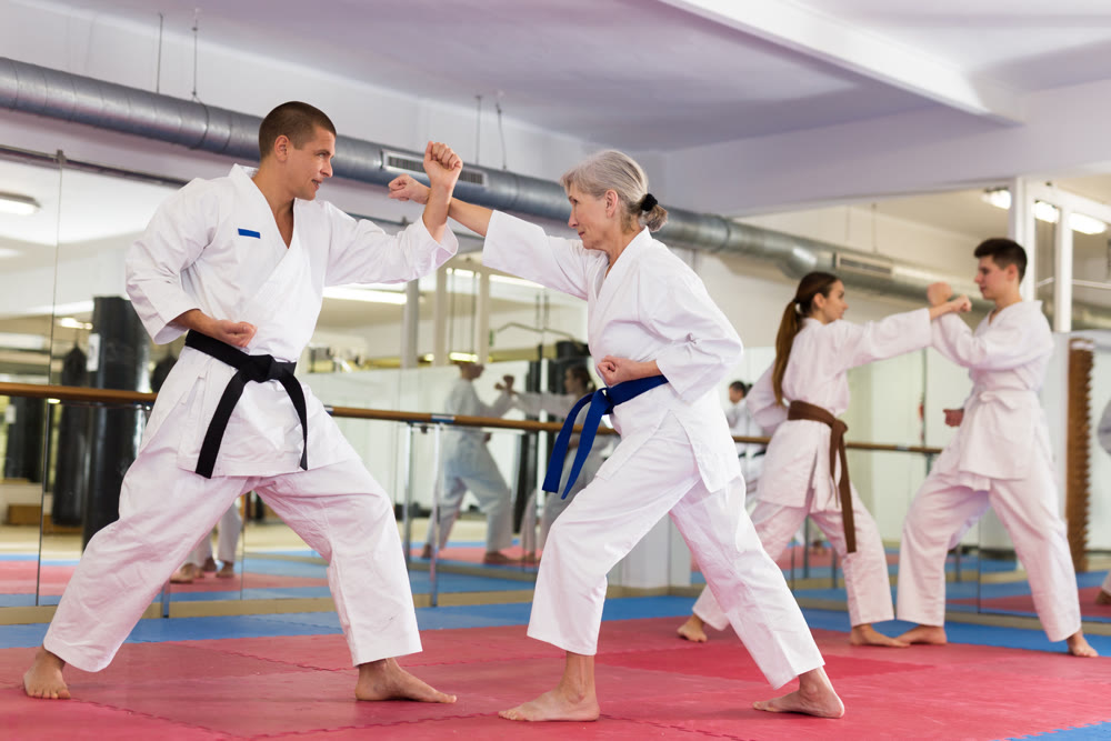 Elderly woman in kimono practicing martial arts techniques with trainer