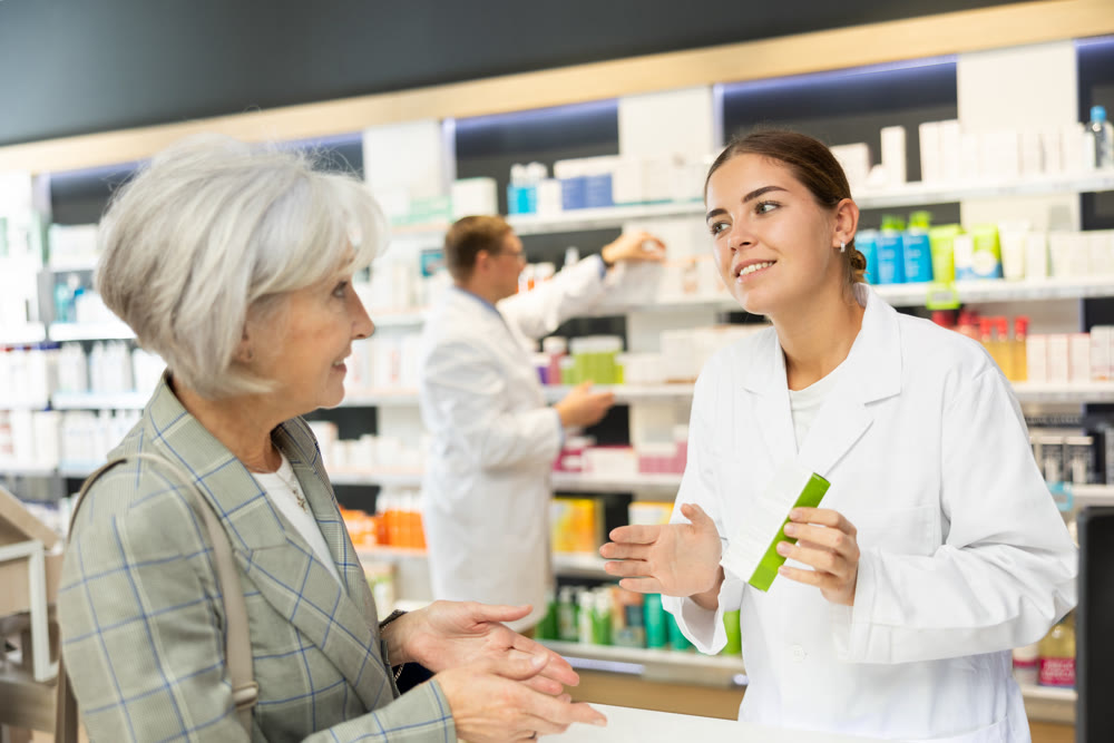 Young female pharmacist consulting old costumer about care product in box
