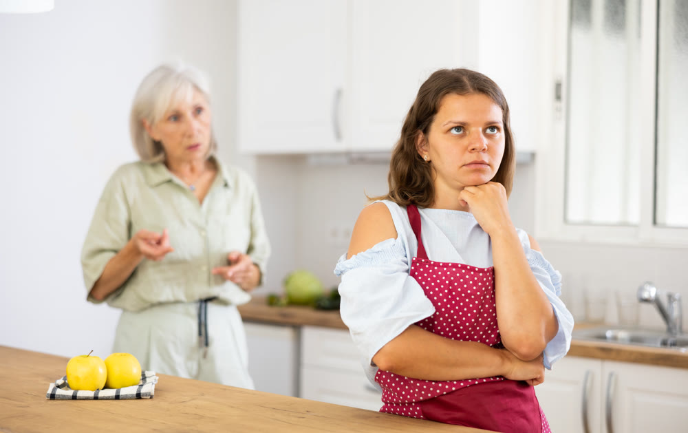 Senior woman scolding her adult daughter cooking breakfast in modern kitchen