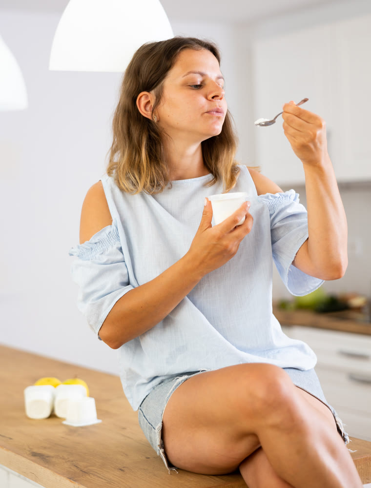 Young woman eating tasty yogurt in kitchen