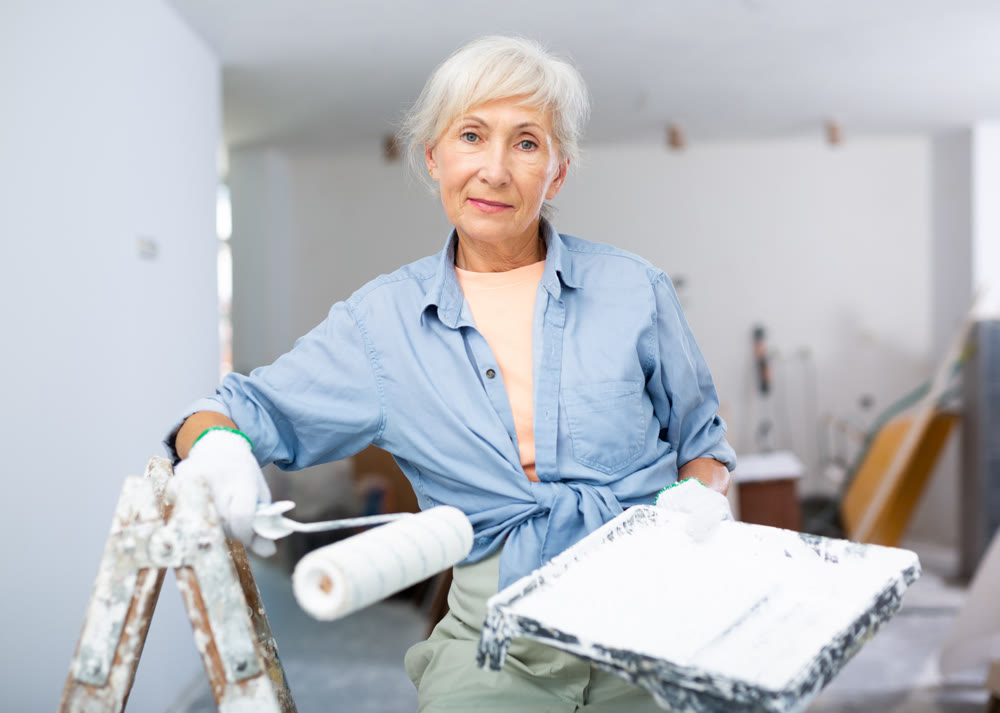 Mature woman painting walls with paint roller in refurbished room
