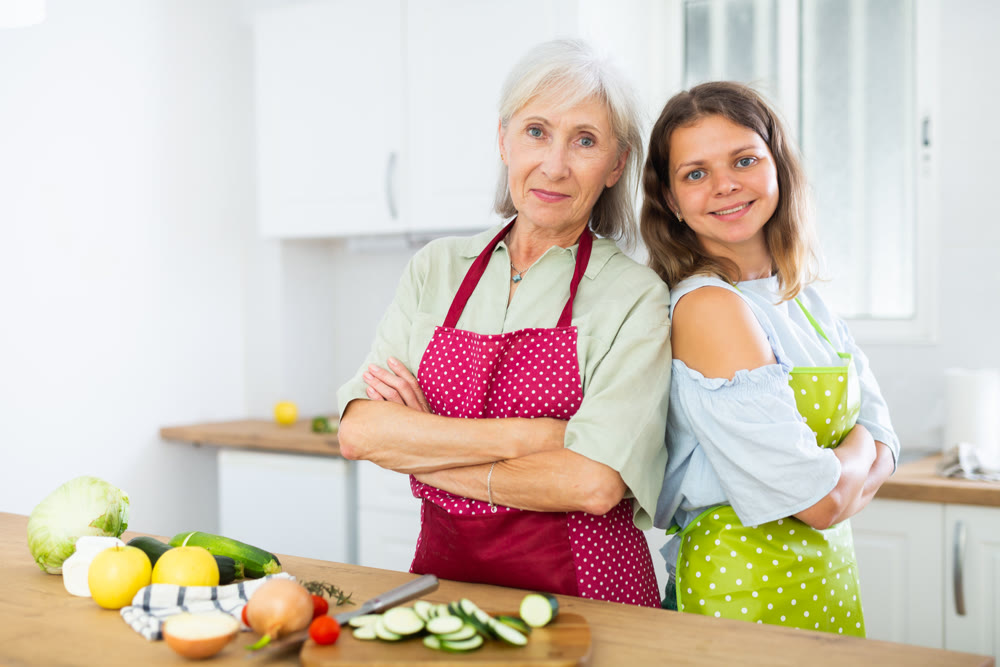 Portrait of elderly woman and her daughter-in-law in an apron in the kitchen - cooking dinner together