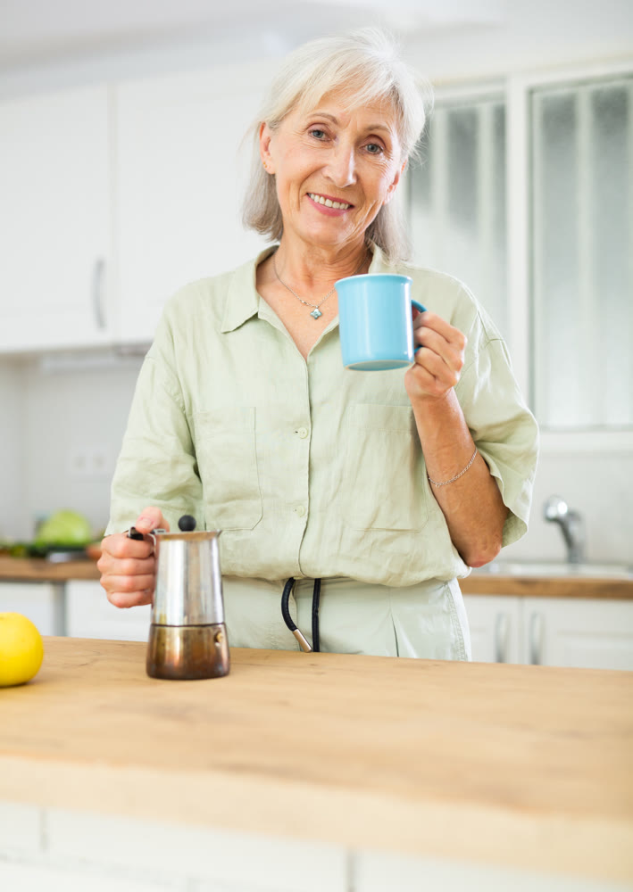 Relaxed elderly woman drinking coffee at kitchen
