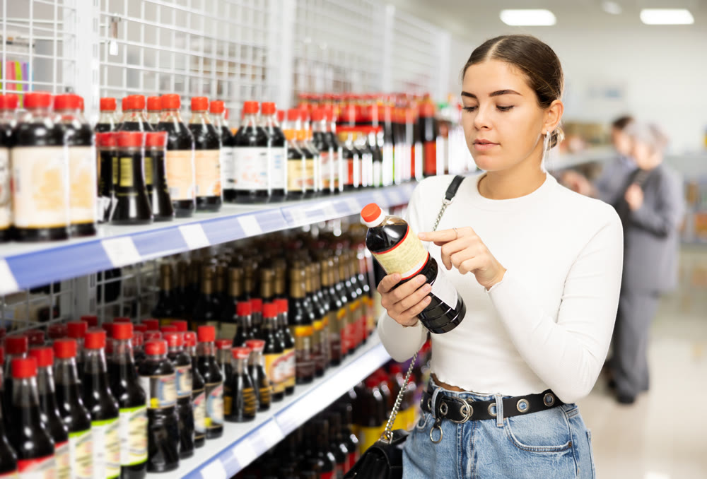 Girl customer is thinking about buying spicy and unusual soy sauce.