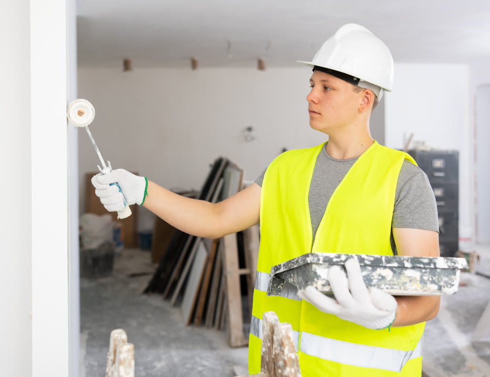 Young man painting wall with paint roller in apartment during repair works