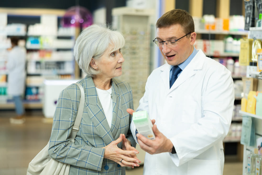 Middle-aged male pharmacist consulting old woman costumer about care product in box